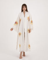Woman modeling a long, lightweight white Turkish towel kimono robe featuring vibrant evil eye motifs on the sleeves and body.