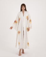 Woman modeling a long, lightweight white Turkish towel kimono robe featuring vibrant evil eye motifs on the sleeves and body.