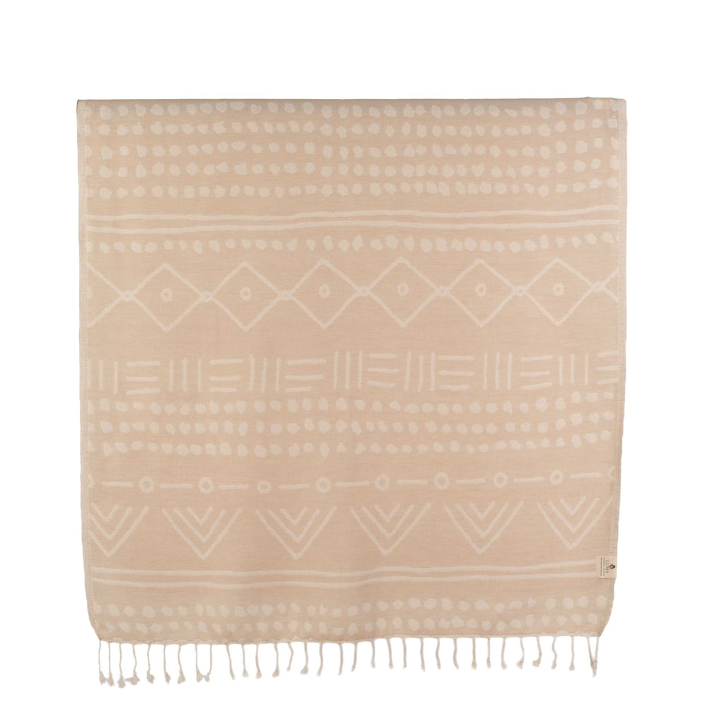 A lightweight Turkish towel with ethnic patterns on a beach at sunset. This super soft, sand-free towel features intricate woven details and fringed edges, held up against a golden ocean backdrop.